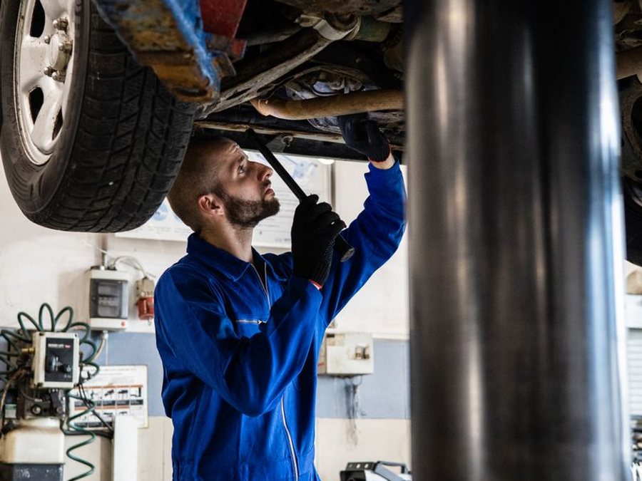 Technician inspecting a vehicle's undercarriage and suspension on a lift