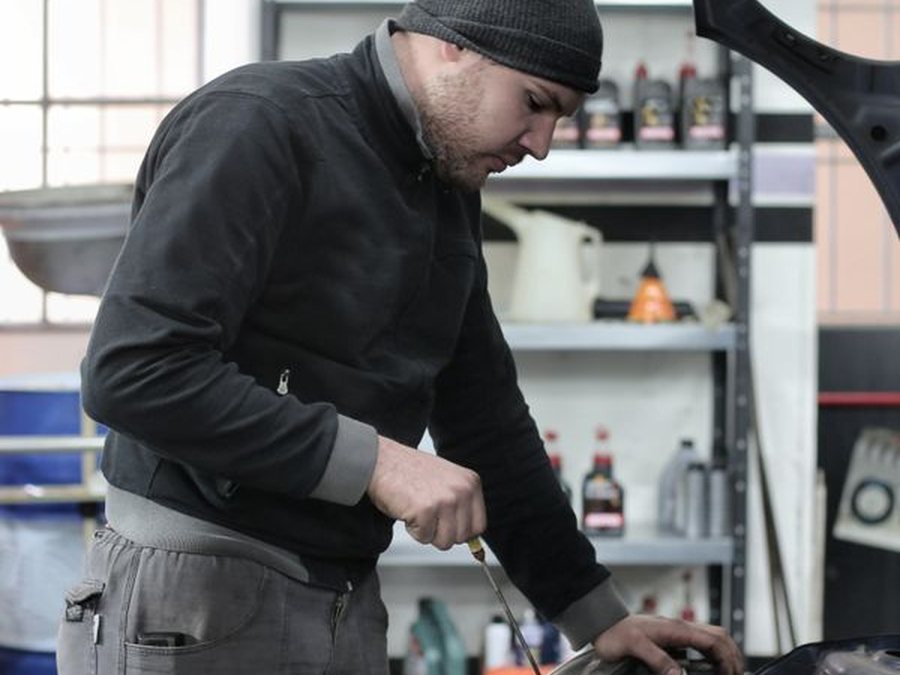 Technician performing a preventive maintenance inspection under the hood